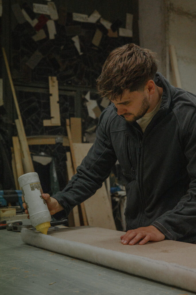 Töötaja valmistab mööbli polstrit ette, kandes pinnale liimi.